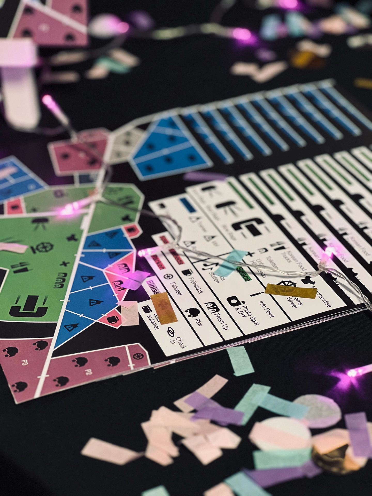 Illustrierter Festivalplan im Spielbrett-Stil für ein K-Pop-Festival mit farbigen Wegfeldern, Symbolen für Stationen wie Check-in, Foodtrucks und Riesenrad, umgeben von Lichterkette und Konfetti