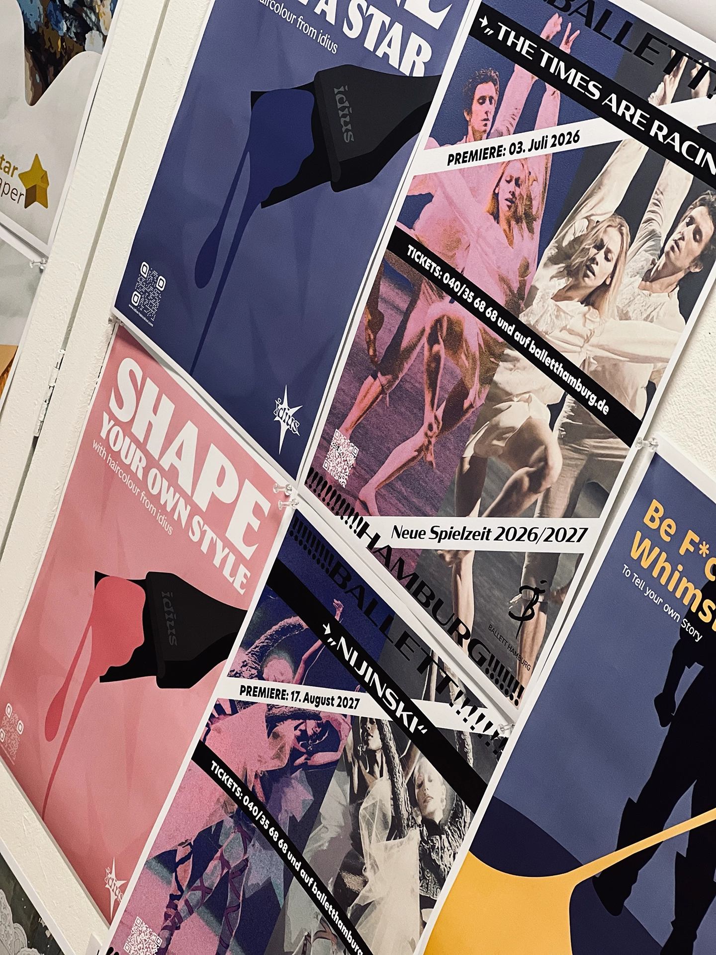 Wand mit mehreren Plakatentwürfen: Haarfarben-Kampagne „idius – Shape your own Style" in Blau- und Rosatönen sowie Spielzeit-Plakate „Ballett Hamburg" zu „Nijinski" und „The Times Are Racing"