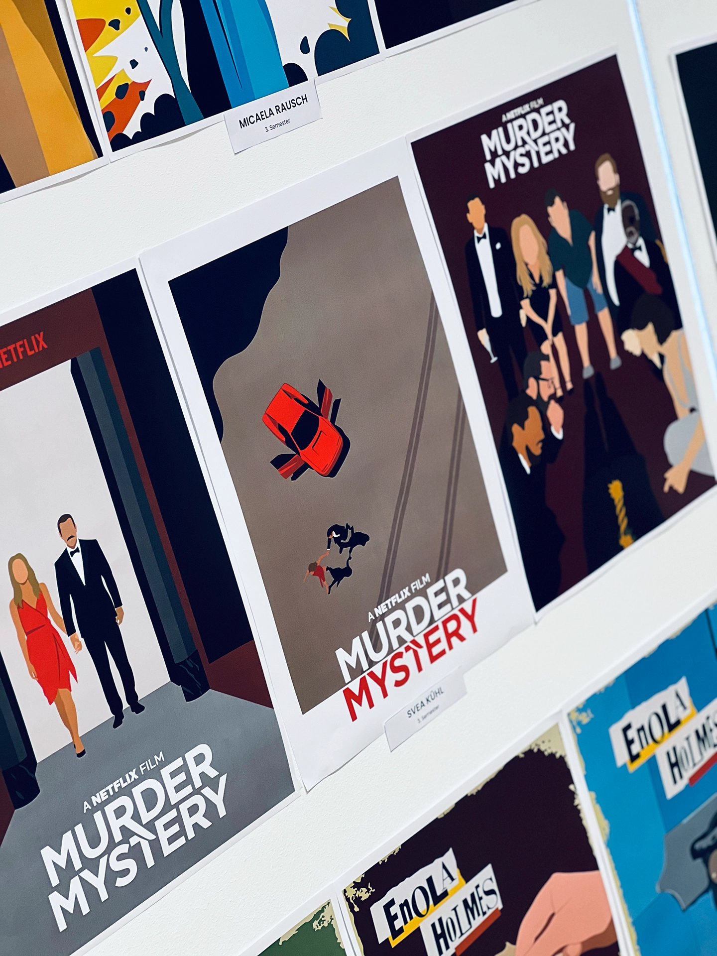Ausstellungswand mit alternativen, flach illustrierten Filmplakaten zu „Murder Mystery" (mehrere Varianten) und „Enola Holmes", daneben Namensschilder der Gestalter:innen